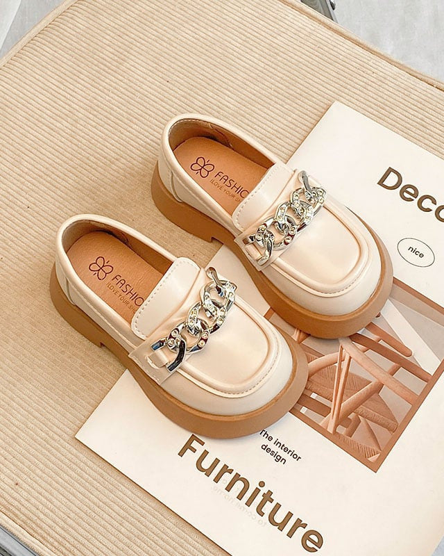 Mocasines escolares de niña en beige con cadena, sobre una revista de decoración Imagen