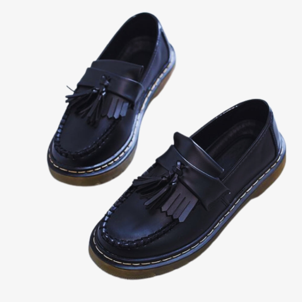 sobre un fondo blanco, un par de mocasines con borlas y flecos de piel sintética para mujer, de color negro