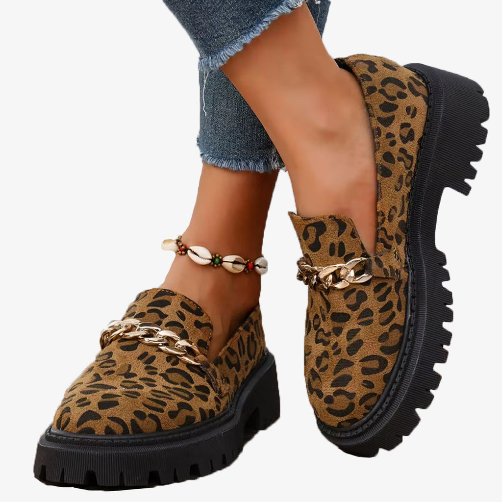 Par de mocasines de ante con estampado de leopardo y cadena, usados con vaqueros y tobillera de conchas