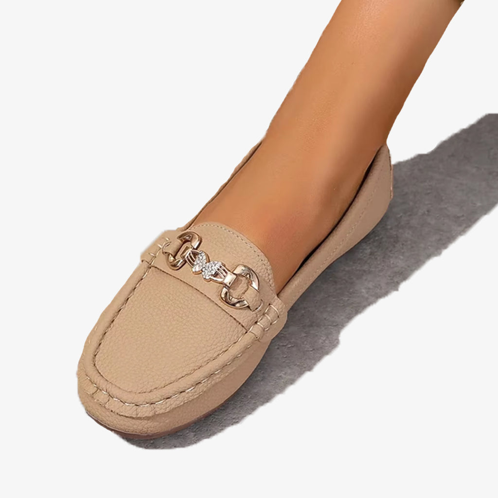 Par de mocasines beige de imitación cuero con cadena y mariposa de strass sobre fondo blanco