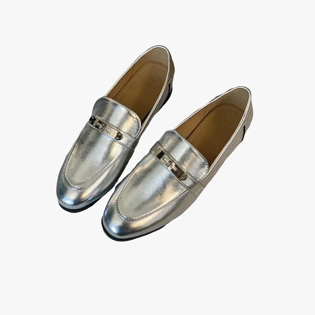 sobre un fondo claro, un par de mocasines plateados de tacón cuadrado para mujer