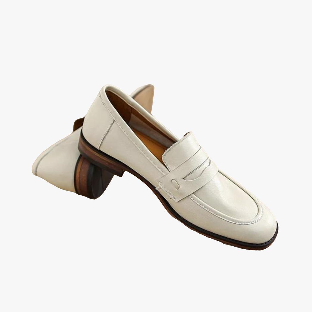 Se ve un par de mocasines beige de suela marrón en piel auténtica sobre un tronco de madera
