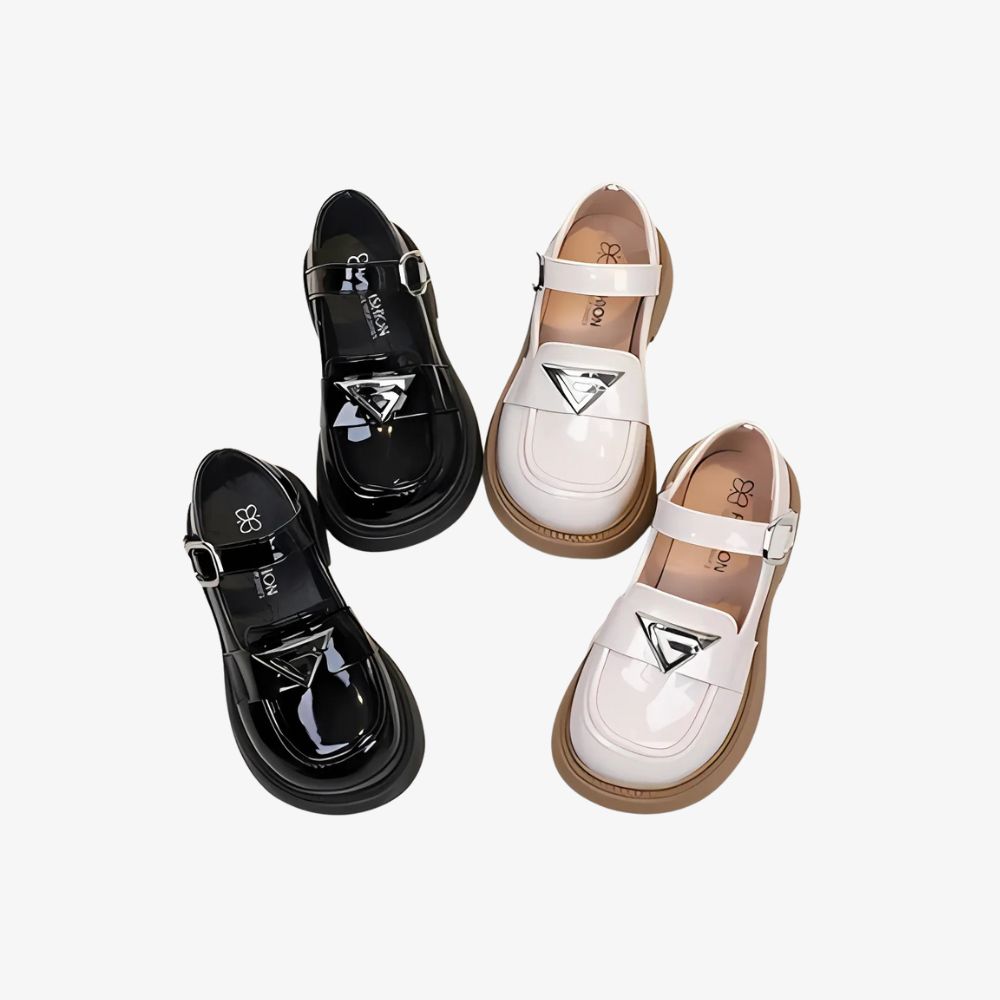 Dos pares de mocasines brillantes en negro y blanco con detalles plateados, sobre fondo gris.