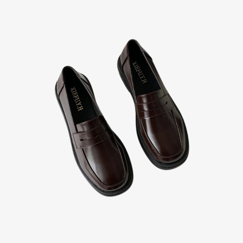 Par de mocasines marrones elegantes, sobre fondo gris claro.