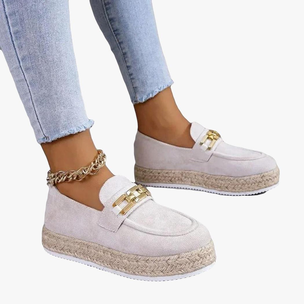 Se ven los pies de una mujer con vaqueros que lleva mocasines de cuña en gamuza sintética de color beige
