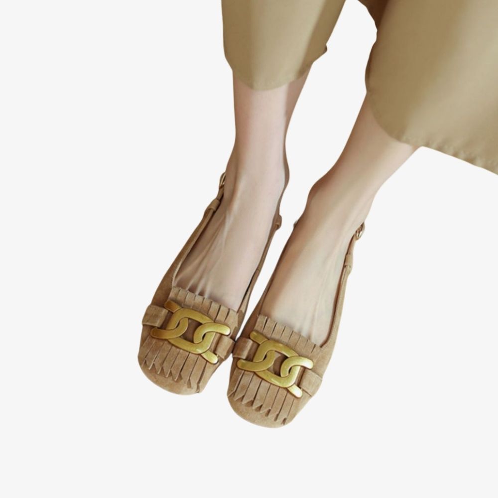 Mocasines beige con flecos y un adorno dorado en el empeine, llevados por una mujer