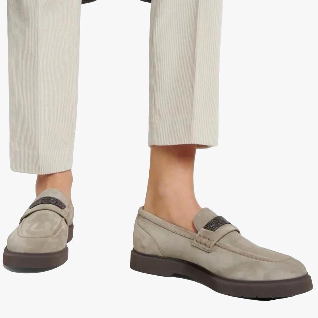 Se ven los pies de una mujer con pantalón de traje beige y mocasines grises de ante auténtico para mujer.