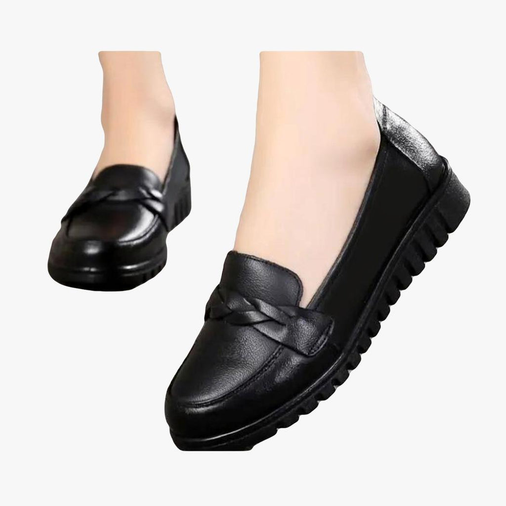 Se ve un par de mocasines negros calzados por una mujer; solo se ven sus pies