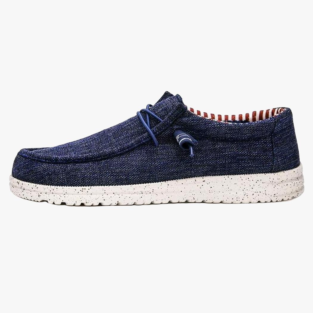 Sobre un fondo blanco se ve un mocasín azul de tejido para hombre