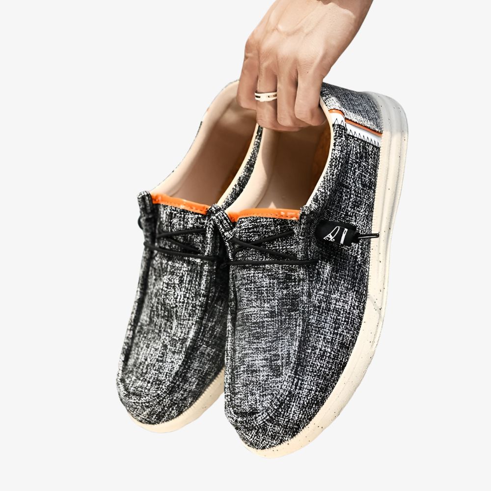 Par de mocasines para hombre de lona de color gris con pequeñas manchas negras y suela blanca.