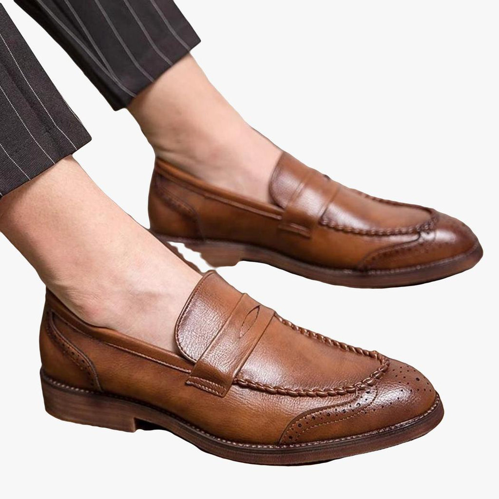 se ve a un hombre sentado, se ven sus pies y lleva mocasines de piel sintética marrones