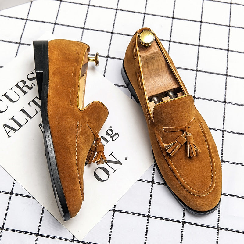 Par de mocasines amarillos con borlas sobre una superficie de cuadros blancos.