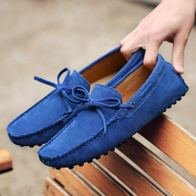 Un par de mocasines azules sostenidos con una mano sobre un banco de madera