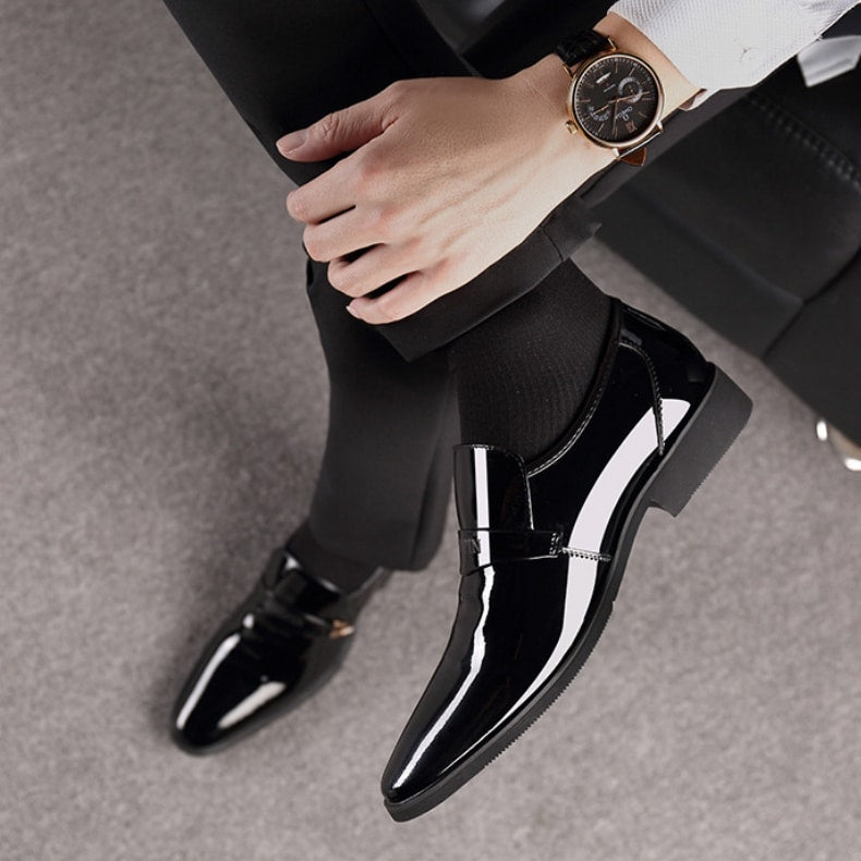 Pies en mocasines de charol negro. Pierna cruzada con un reloj en la muñeca.