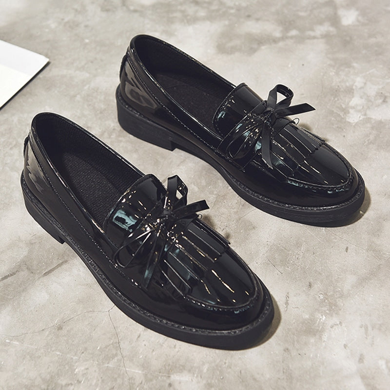 Par de mocasines de charol negro con flecos sobre piso gris