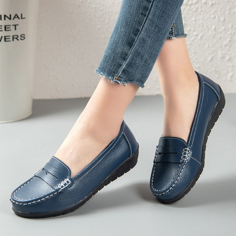 Foto de un par de mocasines de cuero azul llevados por una mujer sobre un suelo gris