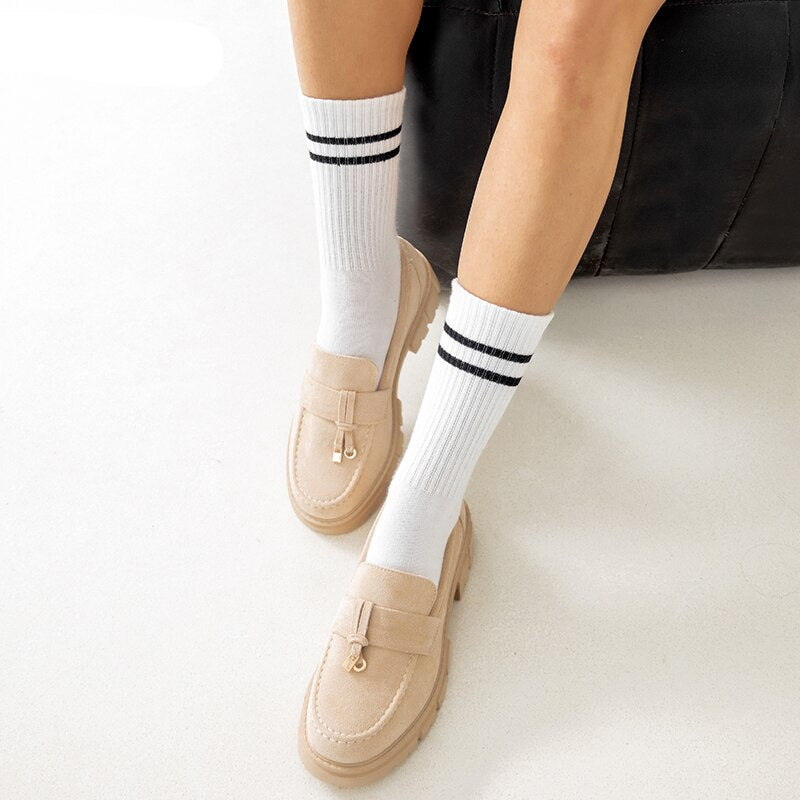 Piernas de mujer con calcetines blancos hasta la rodilla y mocasines de borlas beige