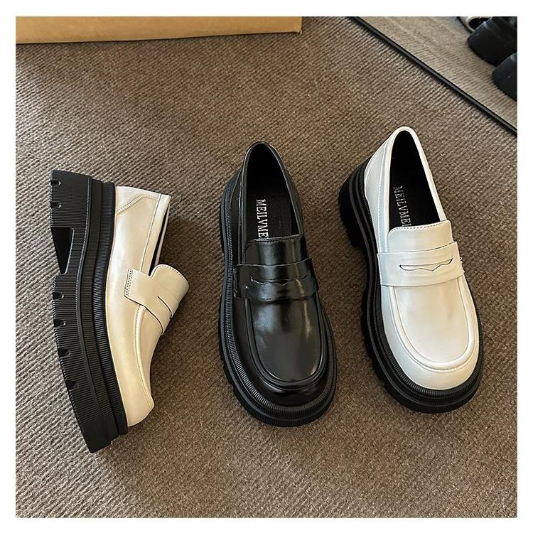 3 mocasines blancos y negros brillan sobre una alfombra gris