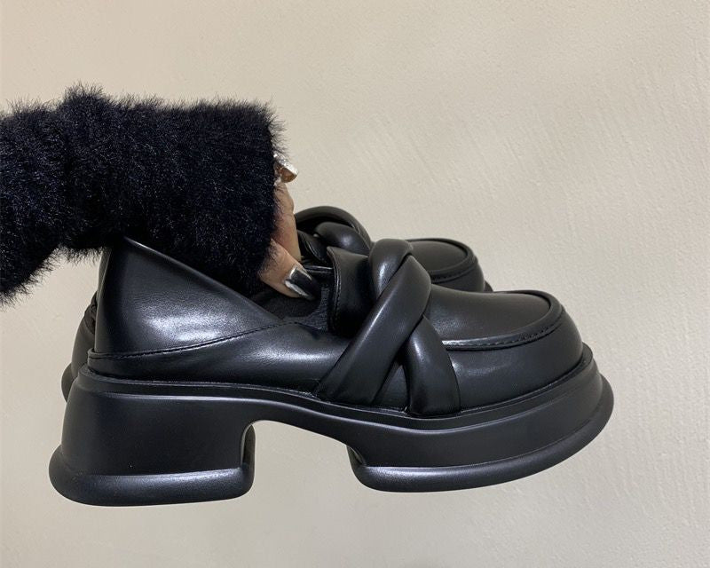 Mocasines de plataforma negros de mujer en piel sintética con fondo beige y una mujer sujetando el par de zapatos