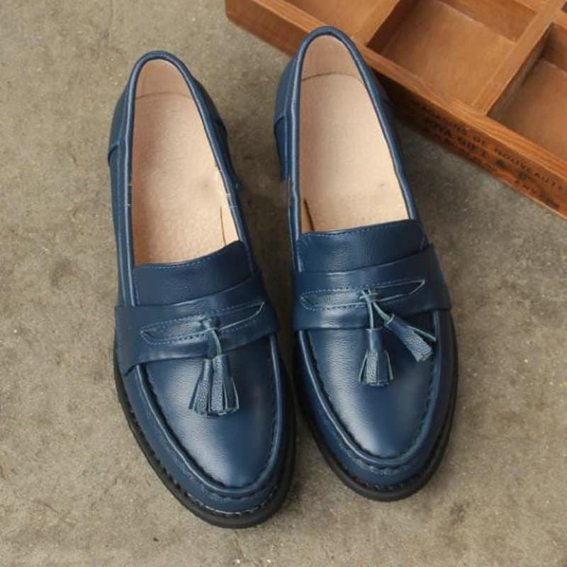 mocasín de cuero azul con tacón y borla en la parte superior, sobre fondo gris