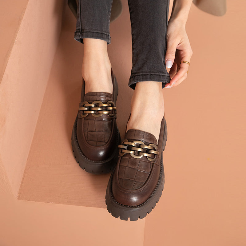 Mocasines de plataforma para mujer en piel marrón con cadena metálica y fondo amarillo