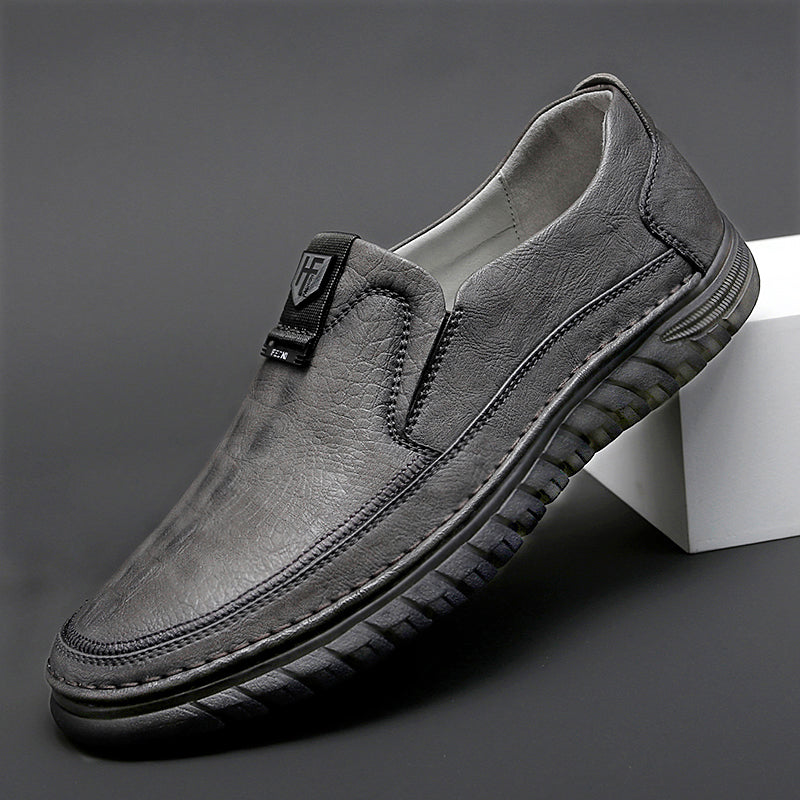 Mocasín ortopédico gris, equilibrado sobre un elemento blanco sobre fondo gris