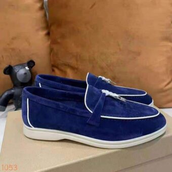 Mocasín en ante azul con ribetes blancos y una borla dura en la parte delantera del zapato que se coloca sobre una caja de zapatos
