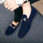 Pies de una persona que lleva mocasines azules con una hebilla dorada en la parte delantera y un reloj en la muñeca