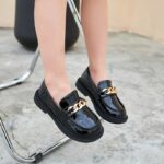 chica con mocasines de poliuretano con una cadena negra