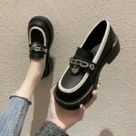 Foto de un par de mocasines negros de plataforma llevados por una mujer en vaqueros sobre un suelo beige