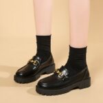 Foto de un par de mocasines negros de plataforma llevados por una mujer sobre un fondo beige
