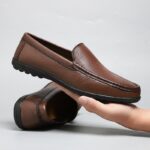 mocasín de cuero marrón en la mano de un hombre con el otro par de zapatos detrás