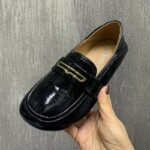 mocasín negro de charol sintético desgastado a mano sobre una pared gris