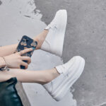 Pies en mocasines blancos con una mano sujetando un teléfono azul