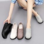 Pierna de mujer con zapatos grises en los pies y otros zapatos a su lado, negros, blancos y marrones