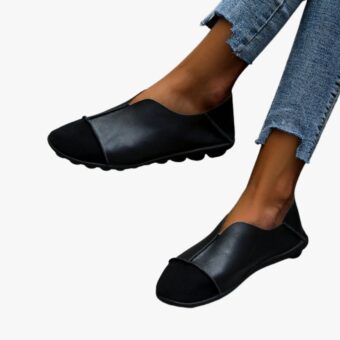 Par de mocasines suaves con puntera redonda en ante negro y cuero liso con costuras visibles llevados con vaqueros sobre un suelo de baldosas gris claro
