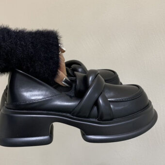 Mocasines de plataforma negros de mujer en piel sintética con fondo beige y una mujer sujetando el par de zapatos