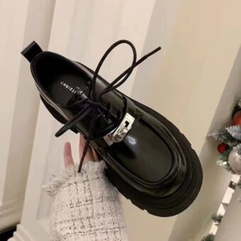 Mano de mujer sujetando un mocasín negro con cordones, en la habitación de una casa