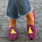 Mujer de pie con las piernas cruzadas en la calle con vaqueros y mocasines de borlas con estampado de leopardo rosa