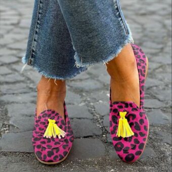 Mujer de pie con las piernas cruzadas en la calle con vaqueros y mocasines de borlas con estampado de leopardo rosa