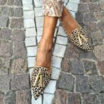 Mujer en la calle con las piernas cruzadas y mocasines de punta de leopardo dorados