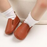 Bebe con calcetines blancos y mocasines marrones lisos de piel sintética