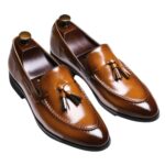 Un par de mocasines masculinos de cuero auténtico con borlas sobre fondo marrón